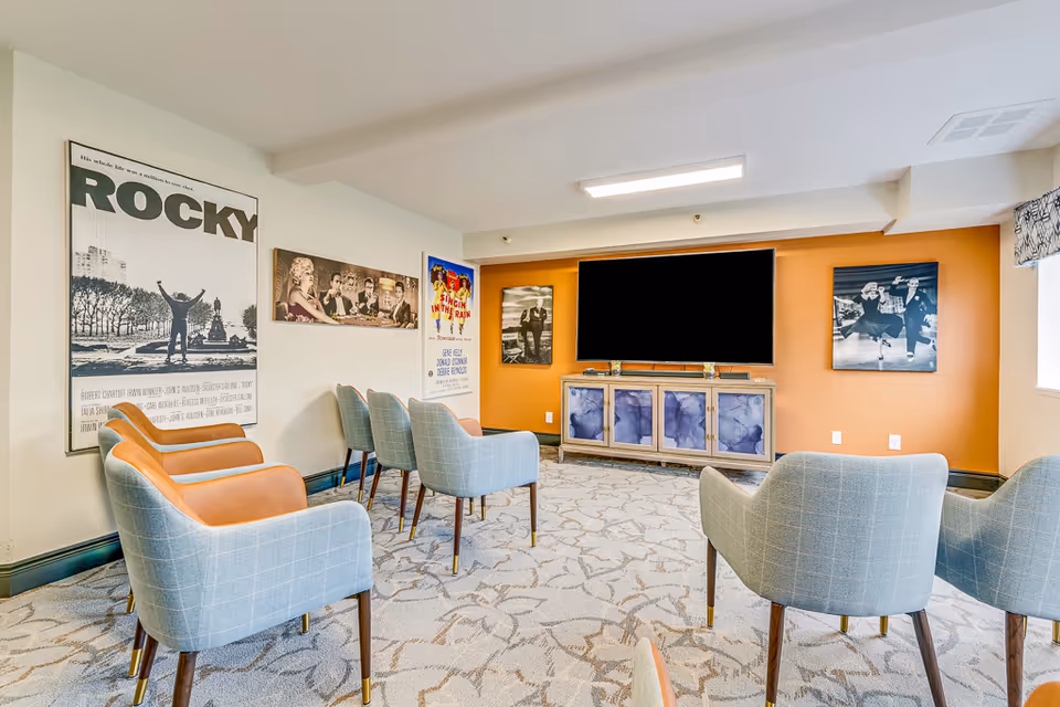 Cozy media room with upholstered chairs arranged facing a large wall-mounted TV and movie posters on the walls.