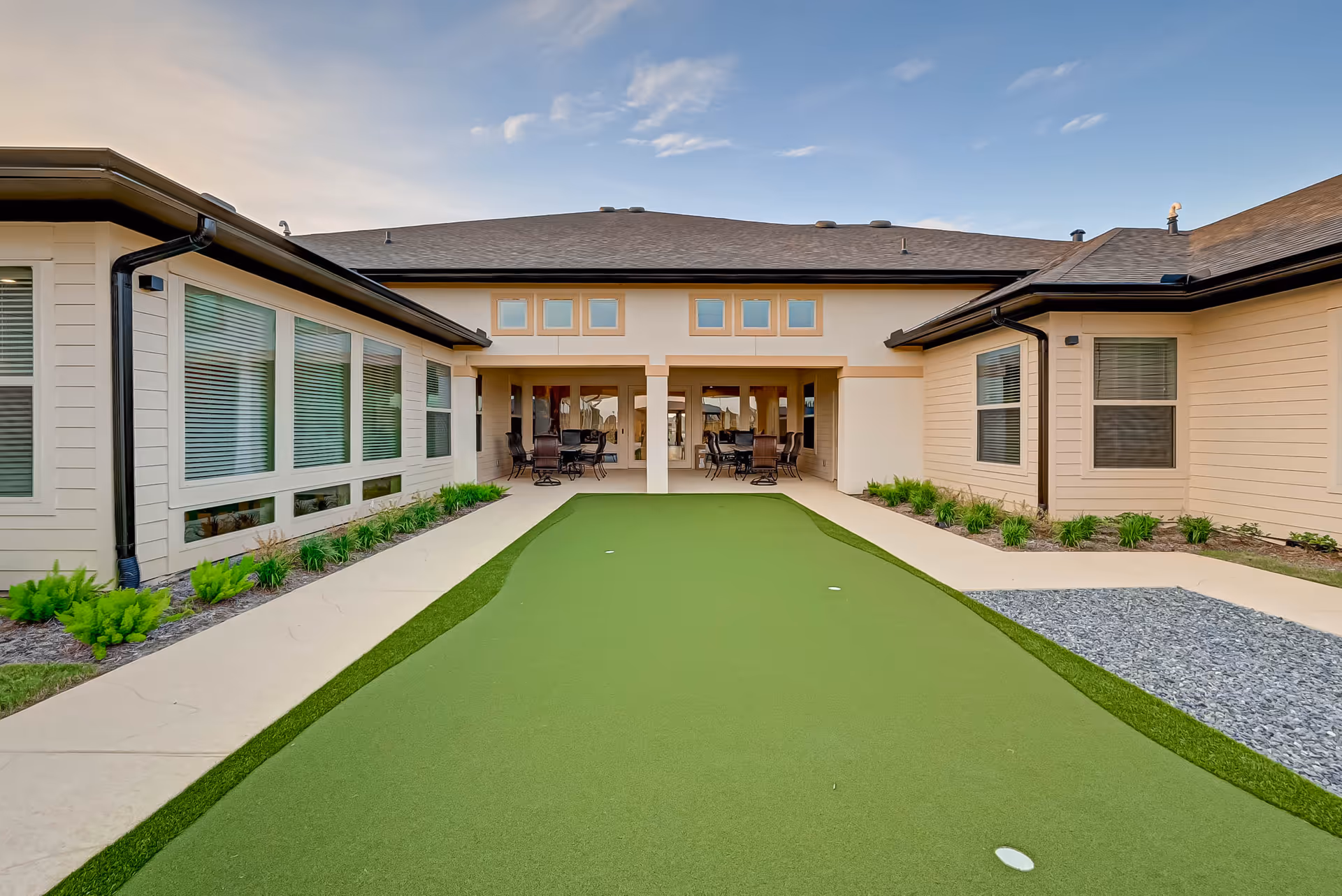 Courtyard putting green leading to a covered patio with outdoor seating between single-story assisted living building wings.