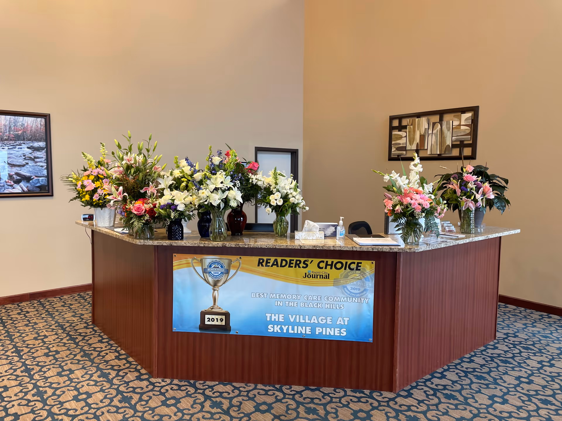 A reception desk in a lobby decorated with multiple bouquets of flowers and a Readers' Choice banner for The Village at Skyline Pines.