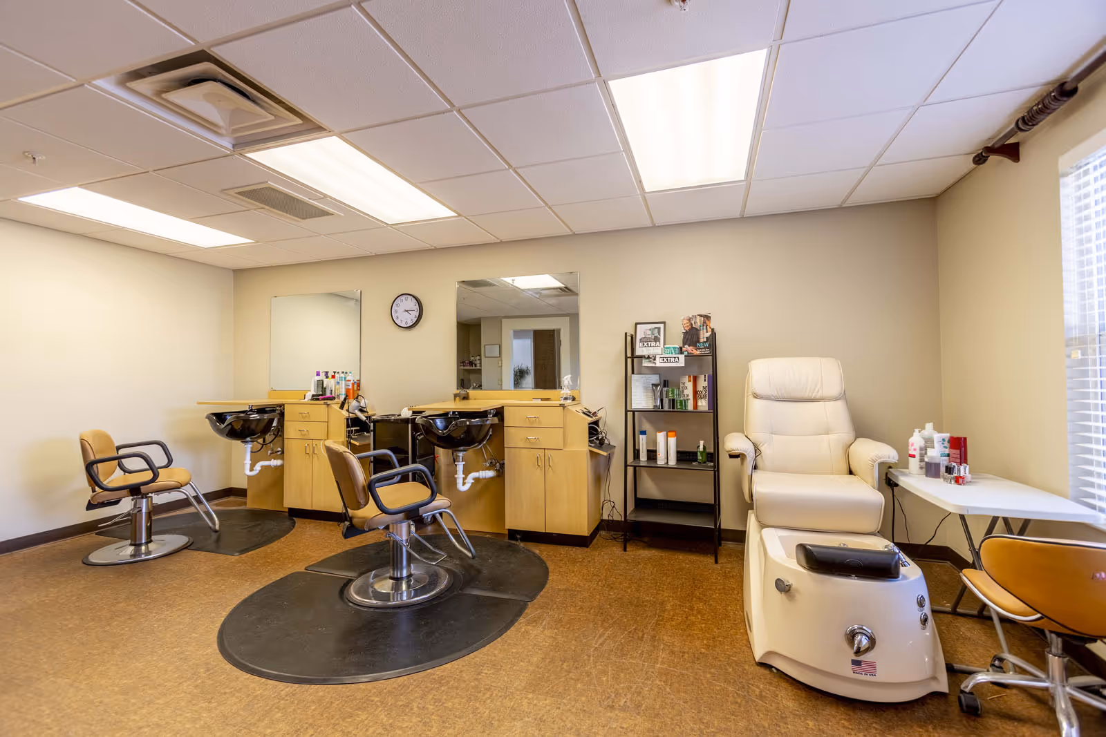 Interior salon room with styling chairs and sinks, mirrors, shelving, and a pedicure chair.