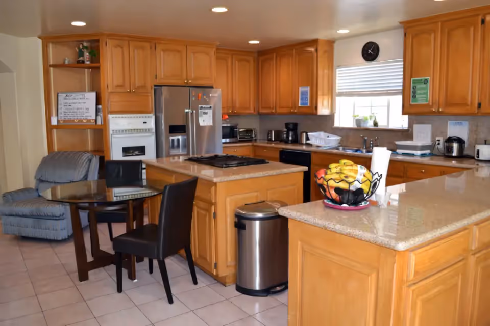 Spacious kitchen with wooden cabinets, a central island, stainless steel refrigerator, dining table and chairs, and a countertop fruit basket.