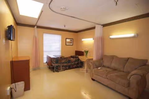 Senior living bedroom with bed, sofa, privacy curtains, small table, and wall TV.