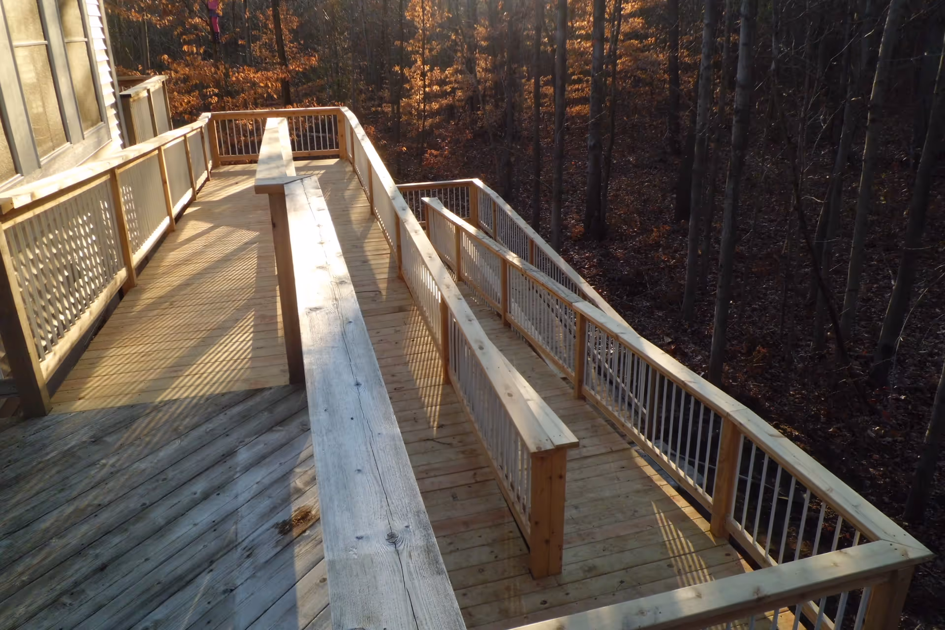 A wooden outdoor ramp and deck attached to a building, surrounded by a forest with tall trees and autumn foliage.