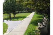 Sidewalk path through a grassy, tree-lined courtyard with a bench on the right.
