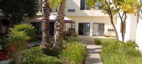 Exterior view of Novellus Clairemont's entrance with a walkway and landscaped greenery.