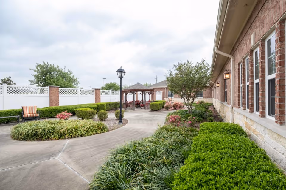 Outdoor landscaped courtyard with concrete walkways, a gazebo, benches, and a brick building facade.