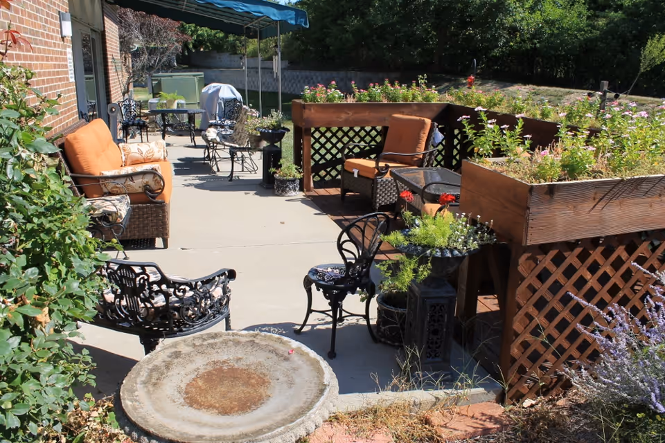 Outdoor patio with cushioned seating, metal chairs and tables, raised wooden planters, and potted plants.