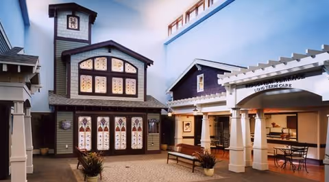 Indoor atrium courtyard with a decorative two-story house, arches, and seating.