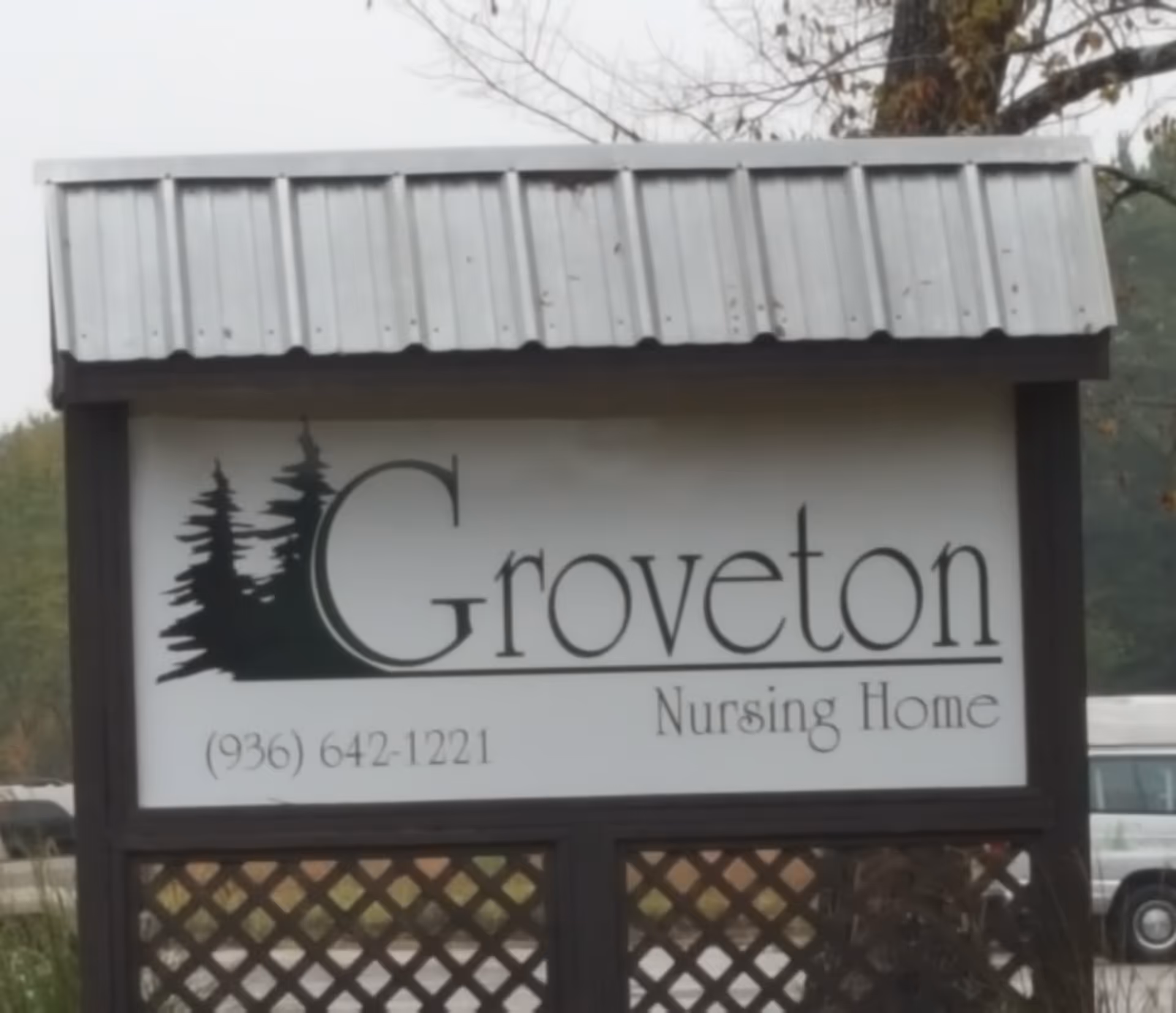 Outdoor sign for Groveton Nursing Home with a metal roof and a white background featuring black text and tree silhouettes.