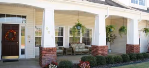 Front entrance of Brookdale Ada with porch seating, hanging plants, and a wreath.