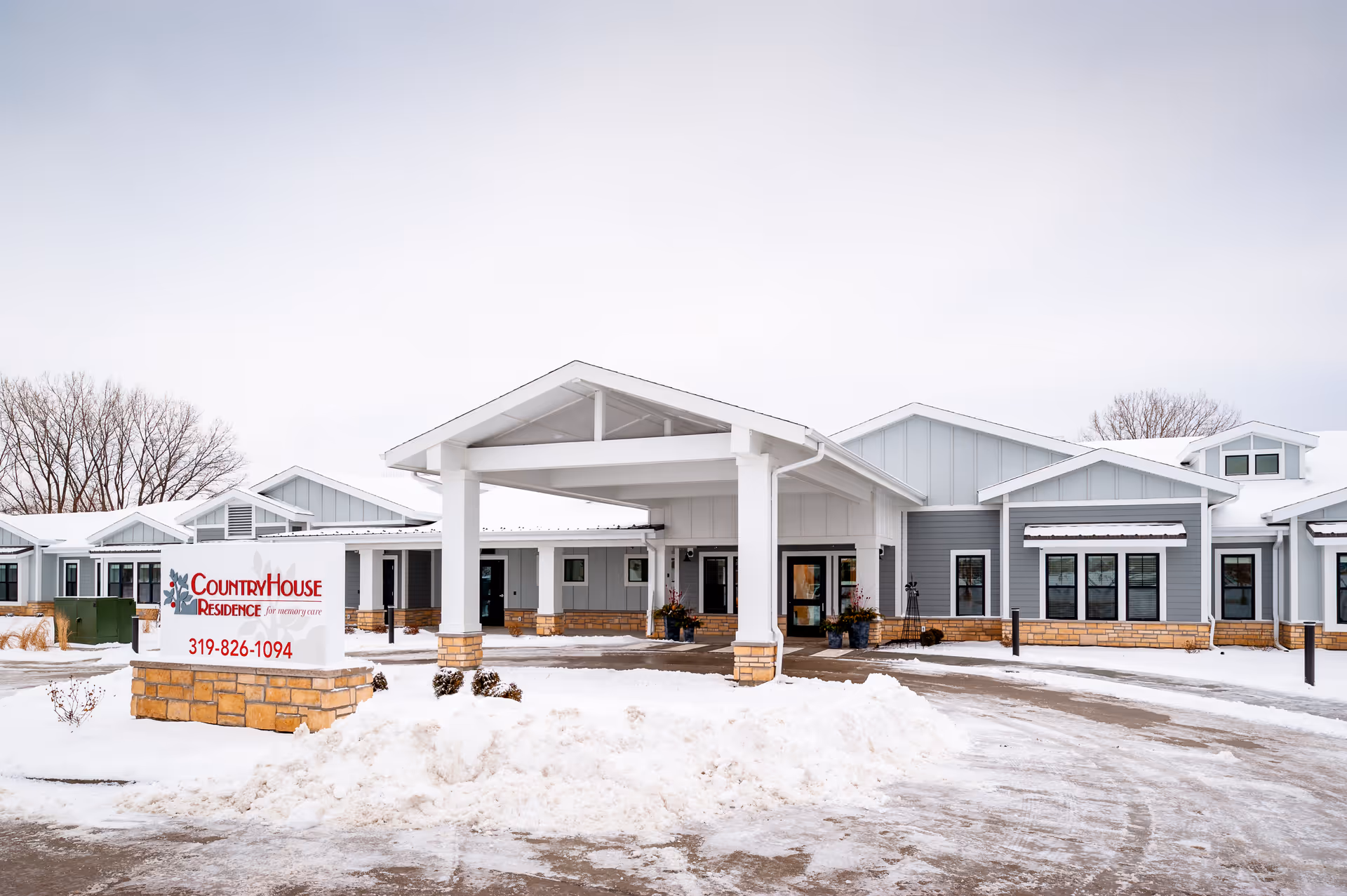 Front exterior of CountryHouse Residence senior living facility with a covered entrance and snow in the driveway.