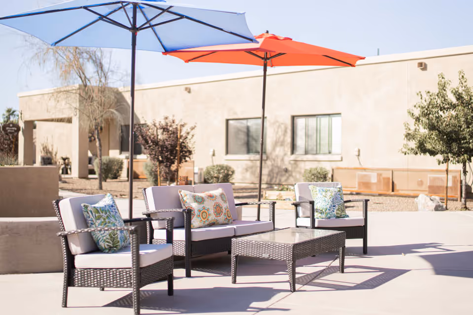 Outdoor patio with wicker seating, a coffee table and colorful umbrellas in front of a single-story building.