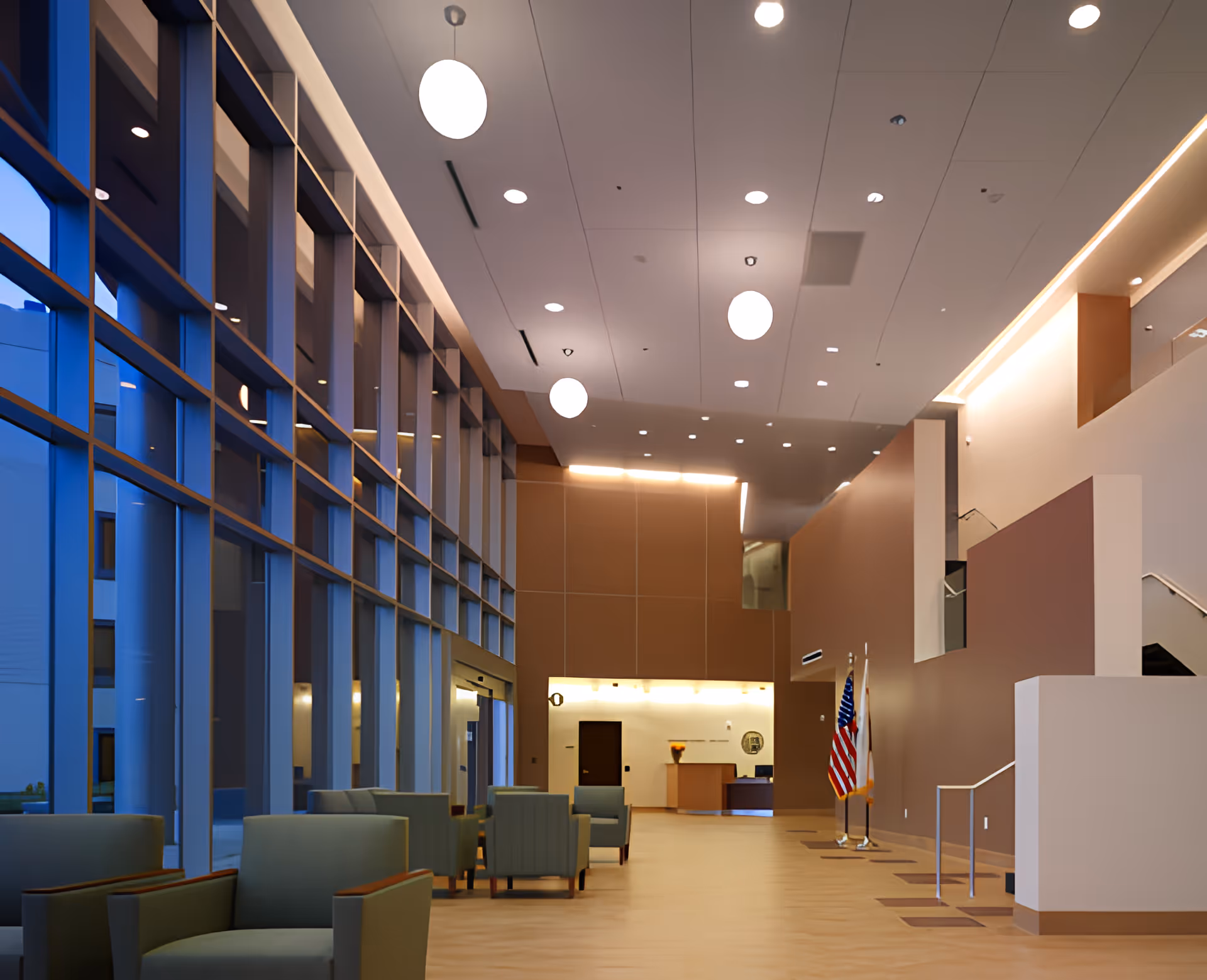 Spacious modern lobby with tall floor-to-ceiling windows, seating, a reception desk, and an American flag.