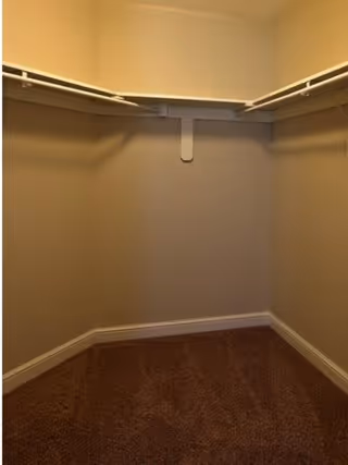 Empty walk-in closet with beige walls, brown carpeted floor, and white wire shelving along two walls.