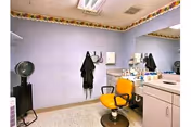 Interior salon area with a yellow styling chair, wall mirror, countertop with supplies, and a hooded hair dryer.