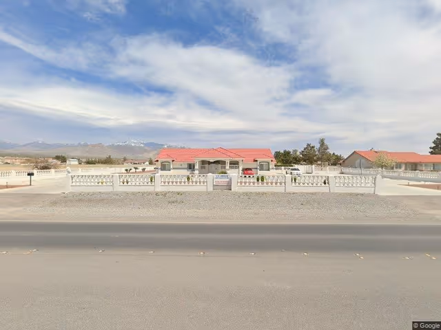Single-story senior care building with a red roof behind a white decorative fence and a road in the foreground.