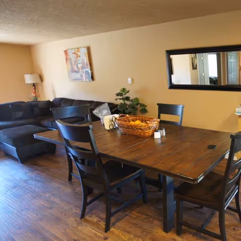 A cozy living room and dining area with a dark wood table, chairs, couch, and mirror.