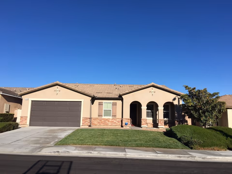 Single-story suburban house front with an attached garage, arched porch, lawn and clear blue sky.