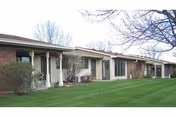 Single-story brick and siding building with multiple entrances and large windows, surrounded by a well-maintained green lawn and leafless trees under a clear sky.