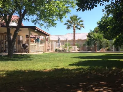 Sunny courtyard at Caring Heart Terrace with green lawn, palm trees, and a fenced patio.