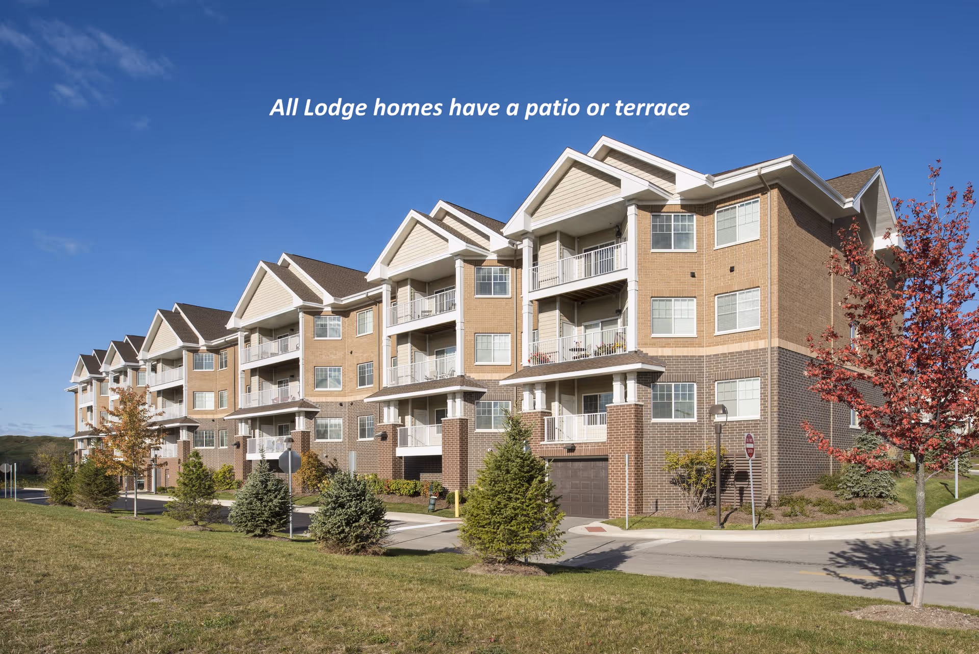 Front exterior of a multi-story senior living apartment building with balconies and landscaped grounds under a blue sky.