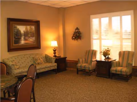 A cozy senior living lounge with sofa, armchairs, lamps, and wall art.