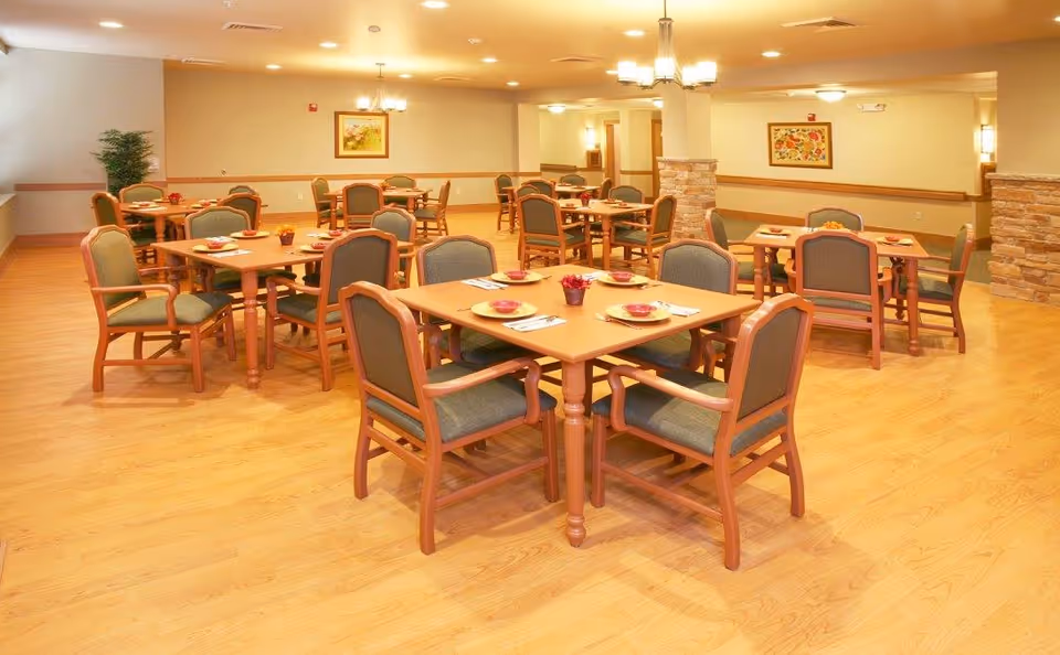 Well-lit dining room with multiple wooden tables and green-upholstered chairs arranged for meals.