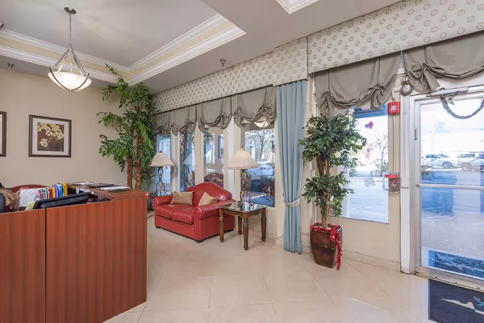 Reception lobby with a wooden front desk, red loveseat, potted plants and large windows by the entrance.