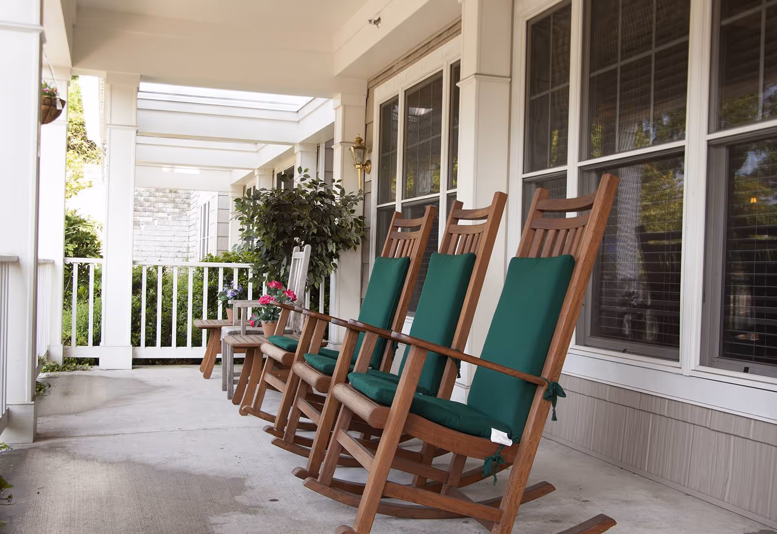 Covered front porch with a row of wooden rocking chairs with green cushions and potted plants.