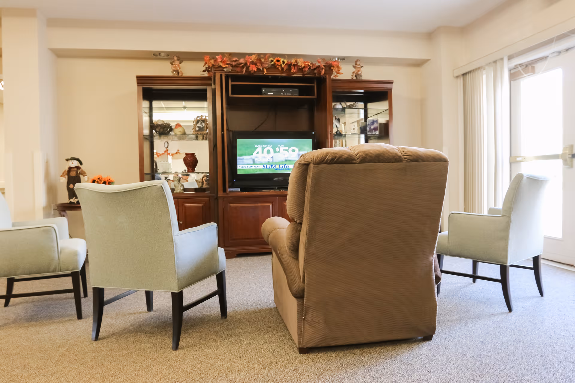 Seating area with armchairs and a recliner facing a wooden entertainment center with a TV in a common room.