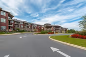 Front entrance of a multi-story senior living building with a curved driveway and landscaped roundabout under a blue sky.