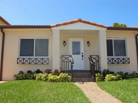 Front entrance of a beige senior living building with a small porch and green lawn.