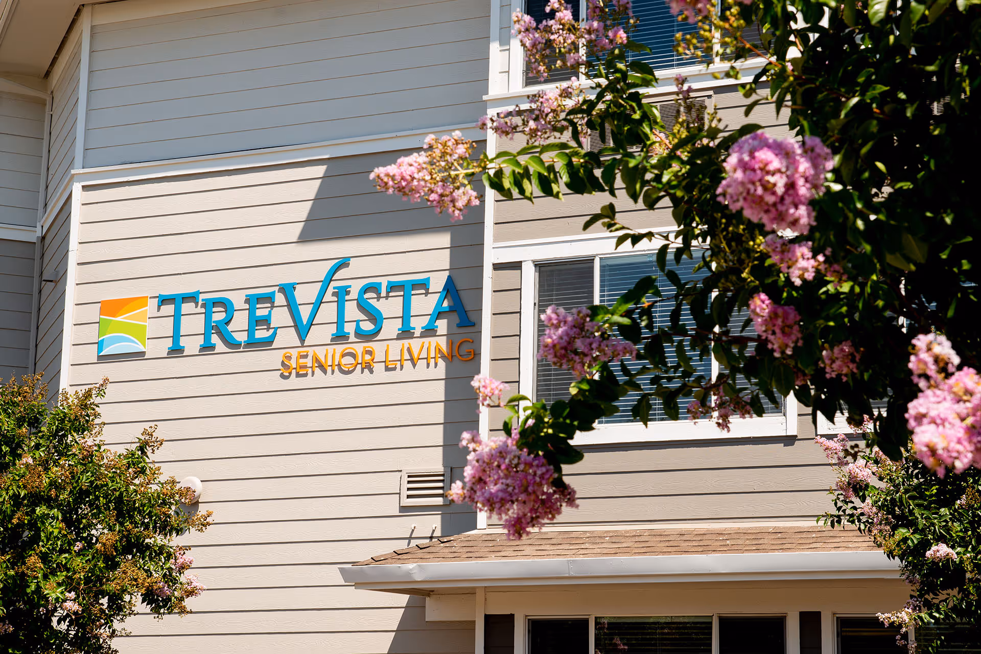 Facade of the TreVista Senior Living building with its sign and pink flowering trees in front.