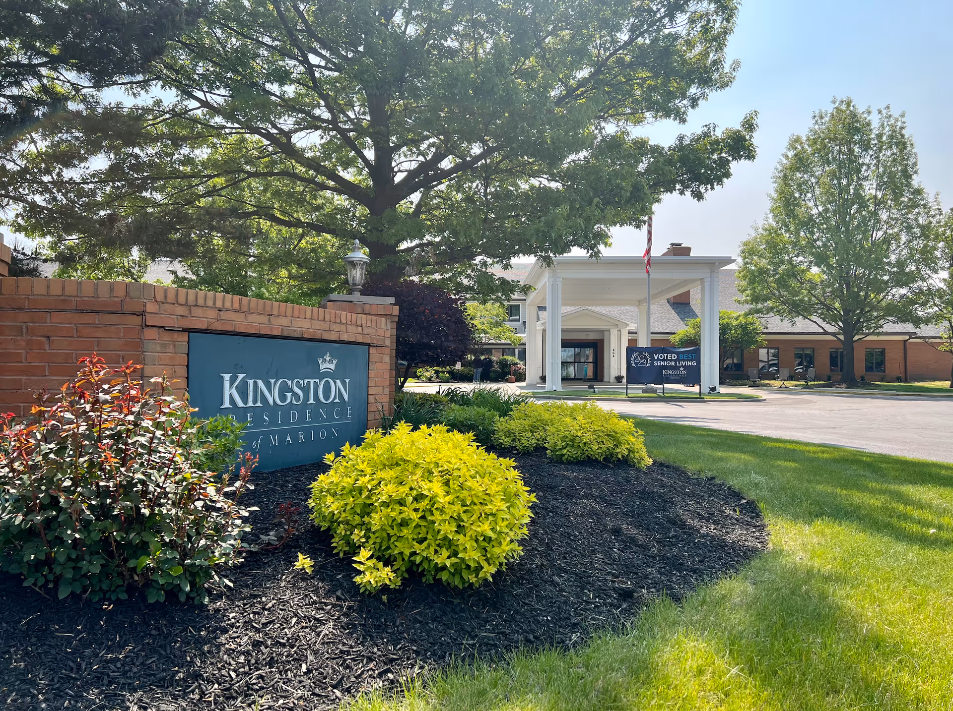 Landscaped front entrance with a brick sign for Kingston Residence of Marion and the facility's covered porte-cochère and driveway.