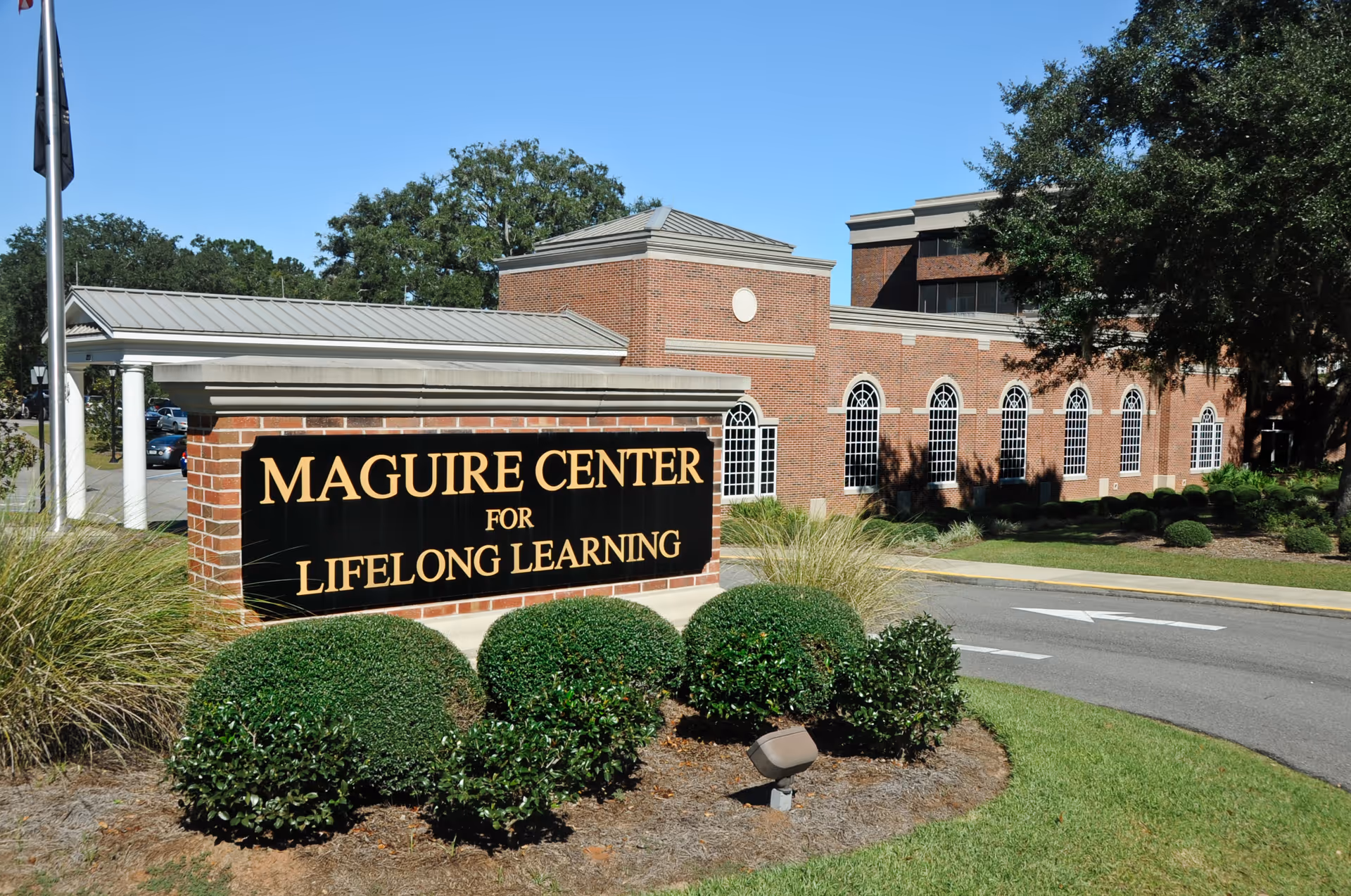 Exterior view of the Maguire Center for Lifelong Learning, a brick building with arched windows, surrounded by greenery and a curved driveway.