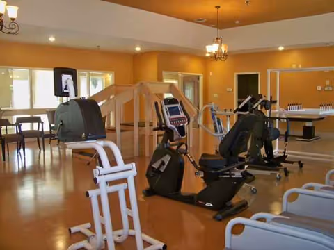Interior gym area with cardio machines and a wooden railing under warm lighting.