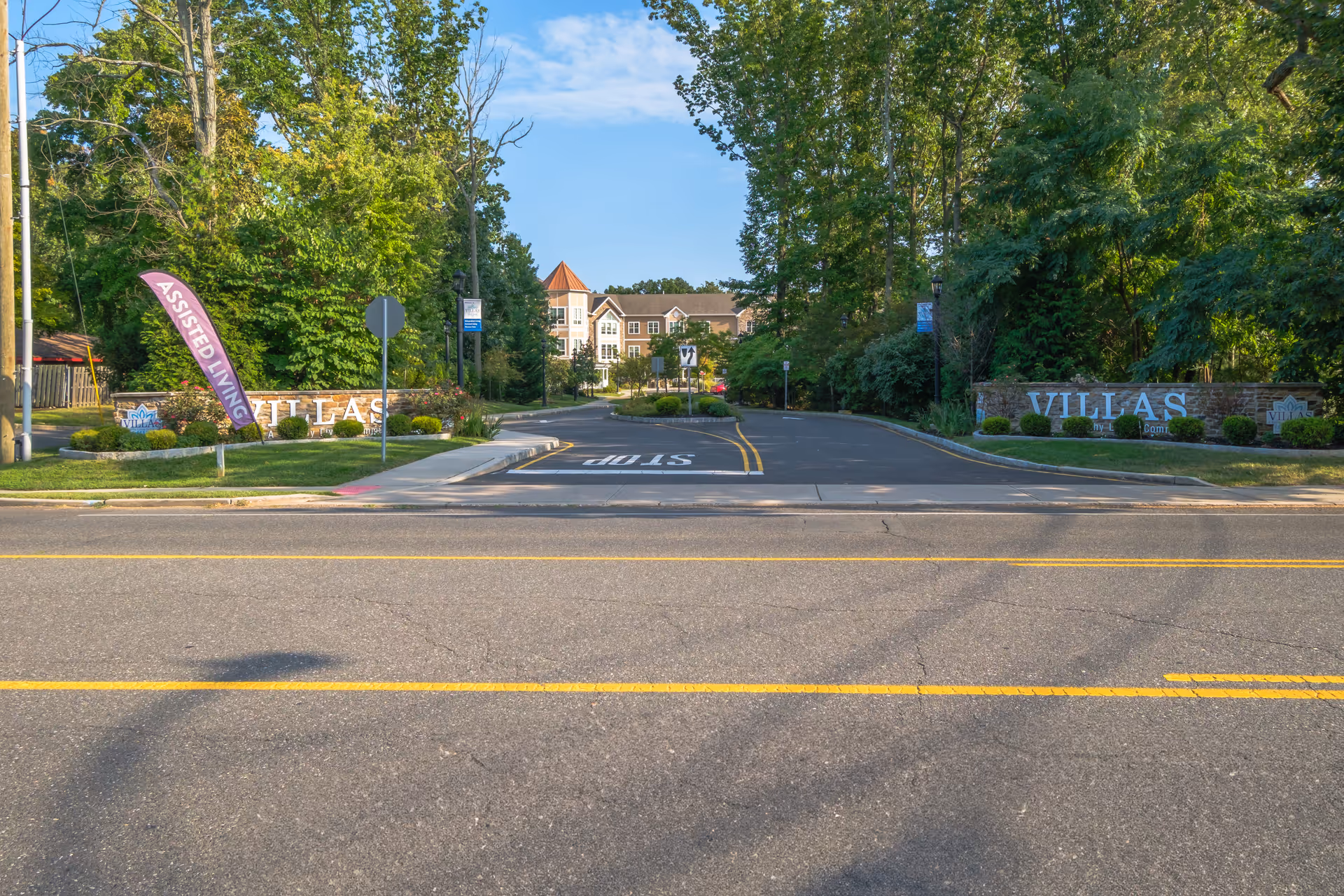 Tree-lined entrance driveway and signage reading 'VILLAS' with the senior living building visible in the background.