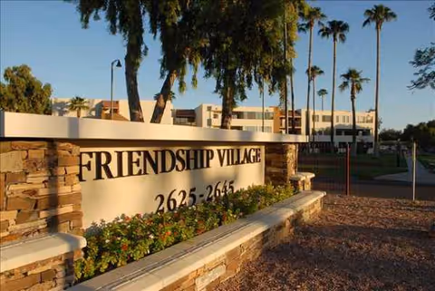 Front view of Friendship Village sign with palm trees and building in Tempe