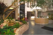 Spacious indoor lobby with a curved reception desk, seating area, and an indoor garden under skylights.