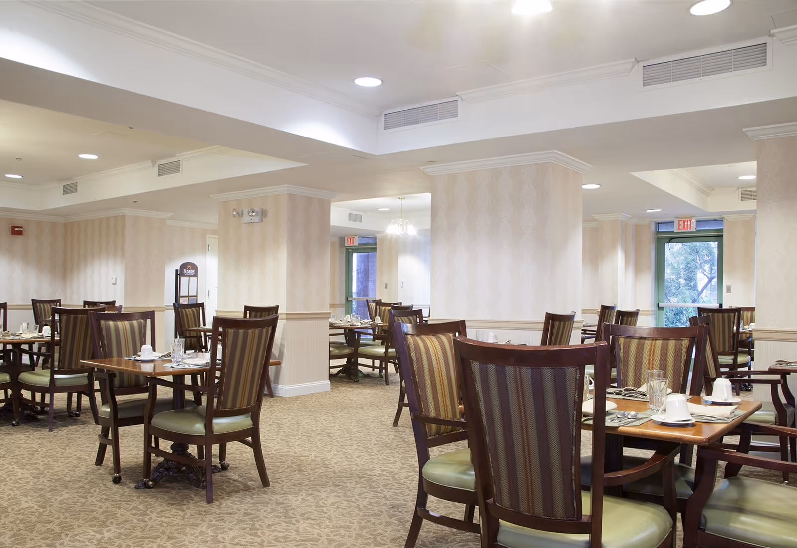 Spacious dining room with multiple wooden tables and upholstered chairs set for meals.