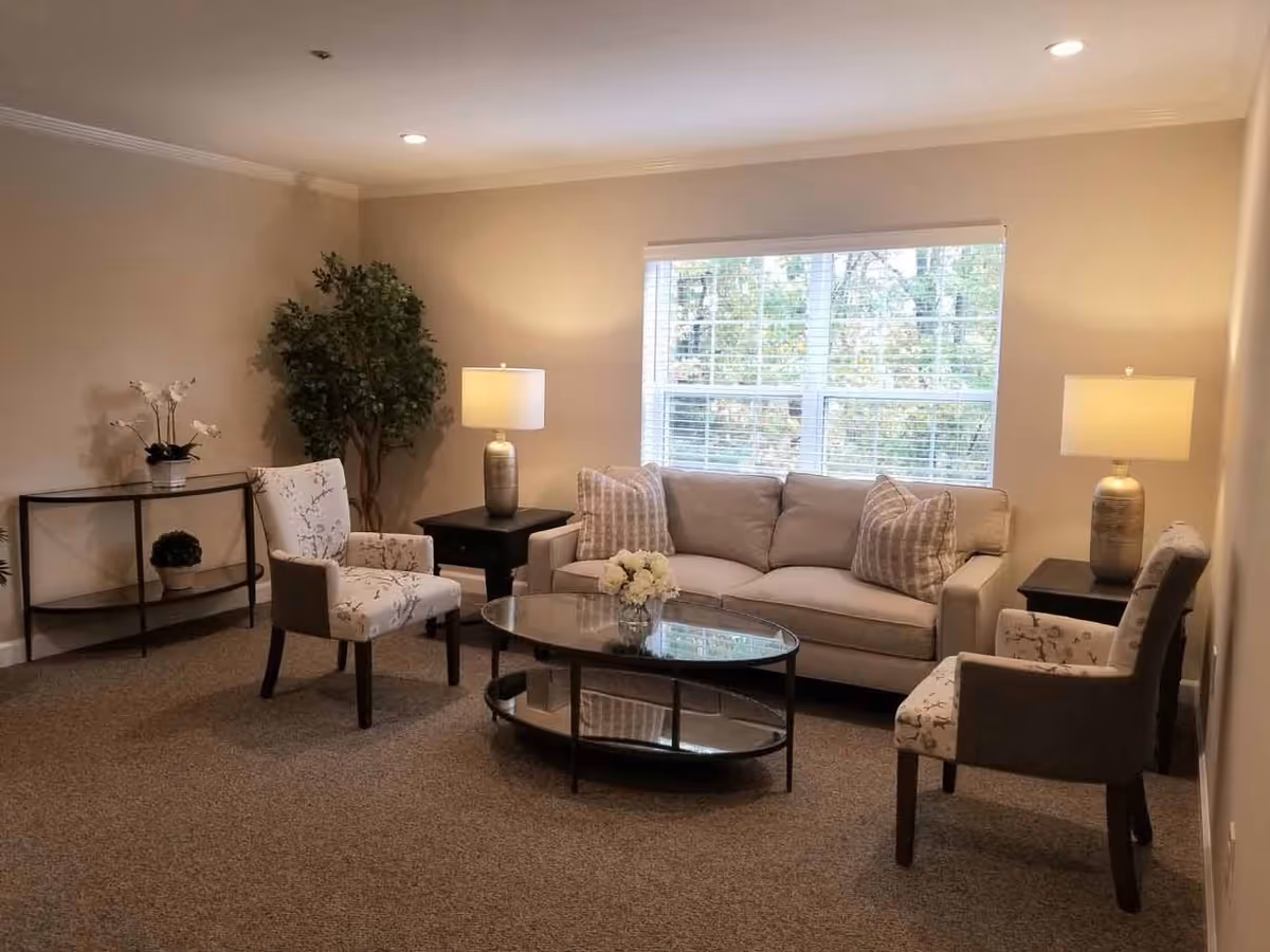 Cozy living room with a sofa, two armchairs, a glass coffee table, lamps, and a large window.