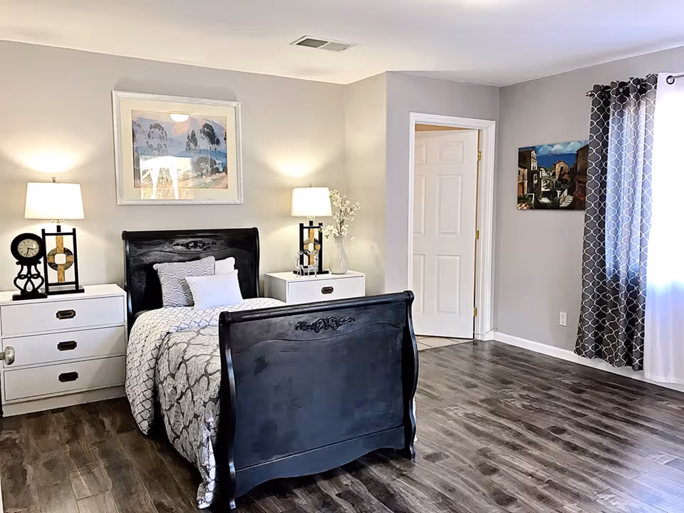 Neatly furnished bedroom featuring a dark wood bed, white nightstands, lamps, and wall art.