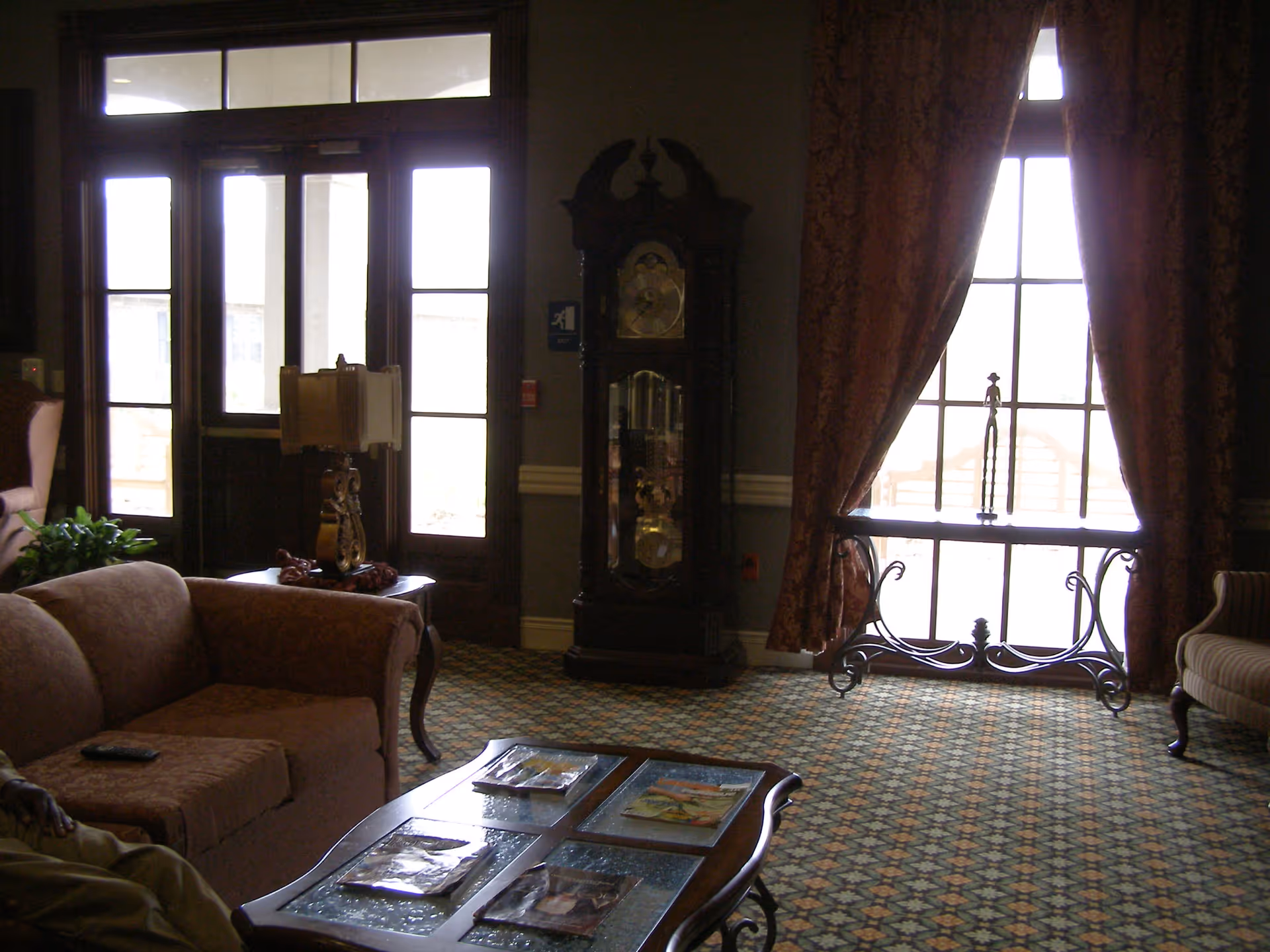 A cozy lounge with sofas, a coffee table, a grandfather clock and large windows with drapes.