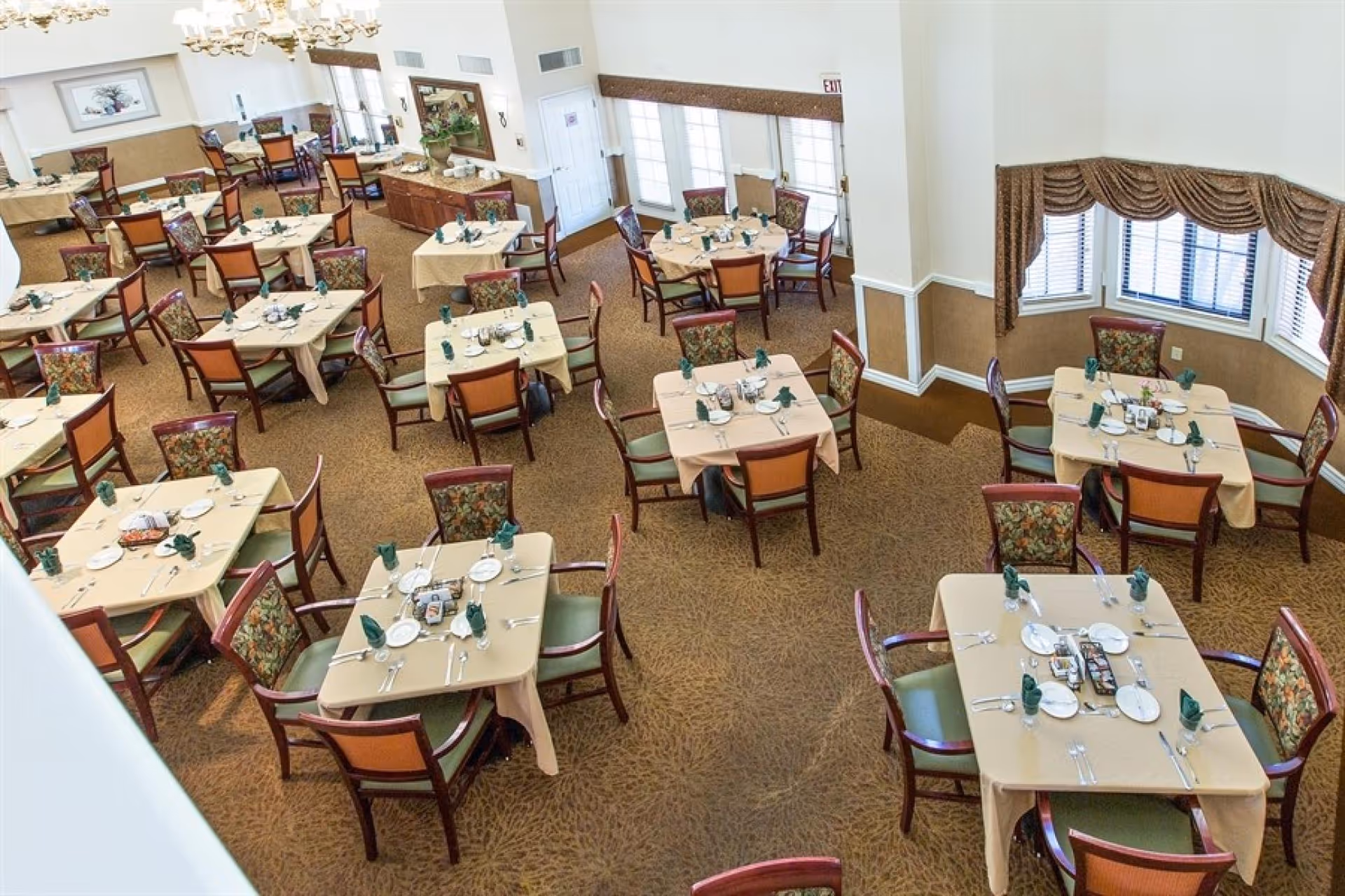 Spacious dining room with multiple tables set with plates, utensils and folded napkins and surrounded by chairs.