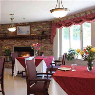 Brick-walled dining room with red tablecloths, chairs, and bright windows.