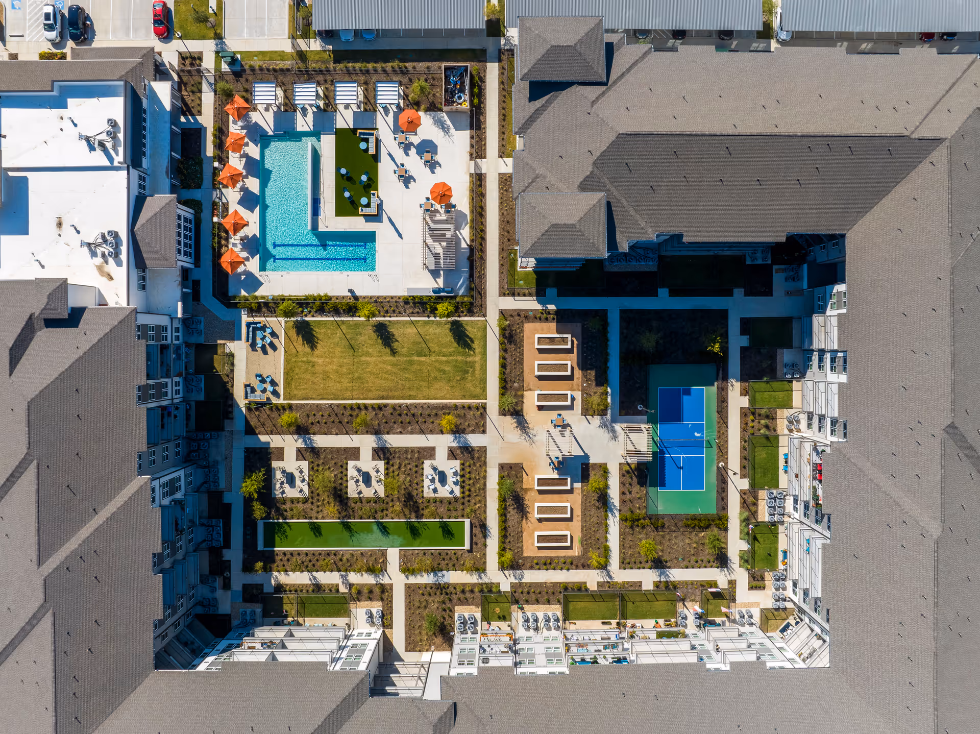 Aerial view of a rectangular senior living courtyard with a swimming pool, sports court, lawns, seating areas and surrounding buildings.