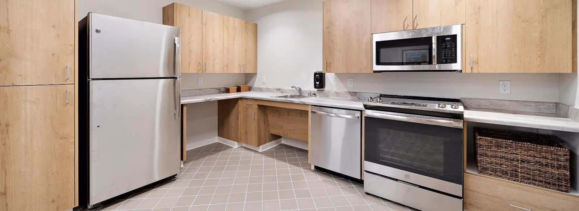 Modern kitchen with stainless steel refrigerator, oven, microwave and dishwasher, light wood cabinets and tiled floor.