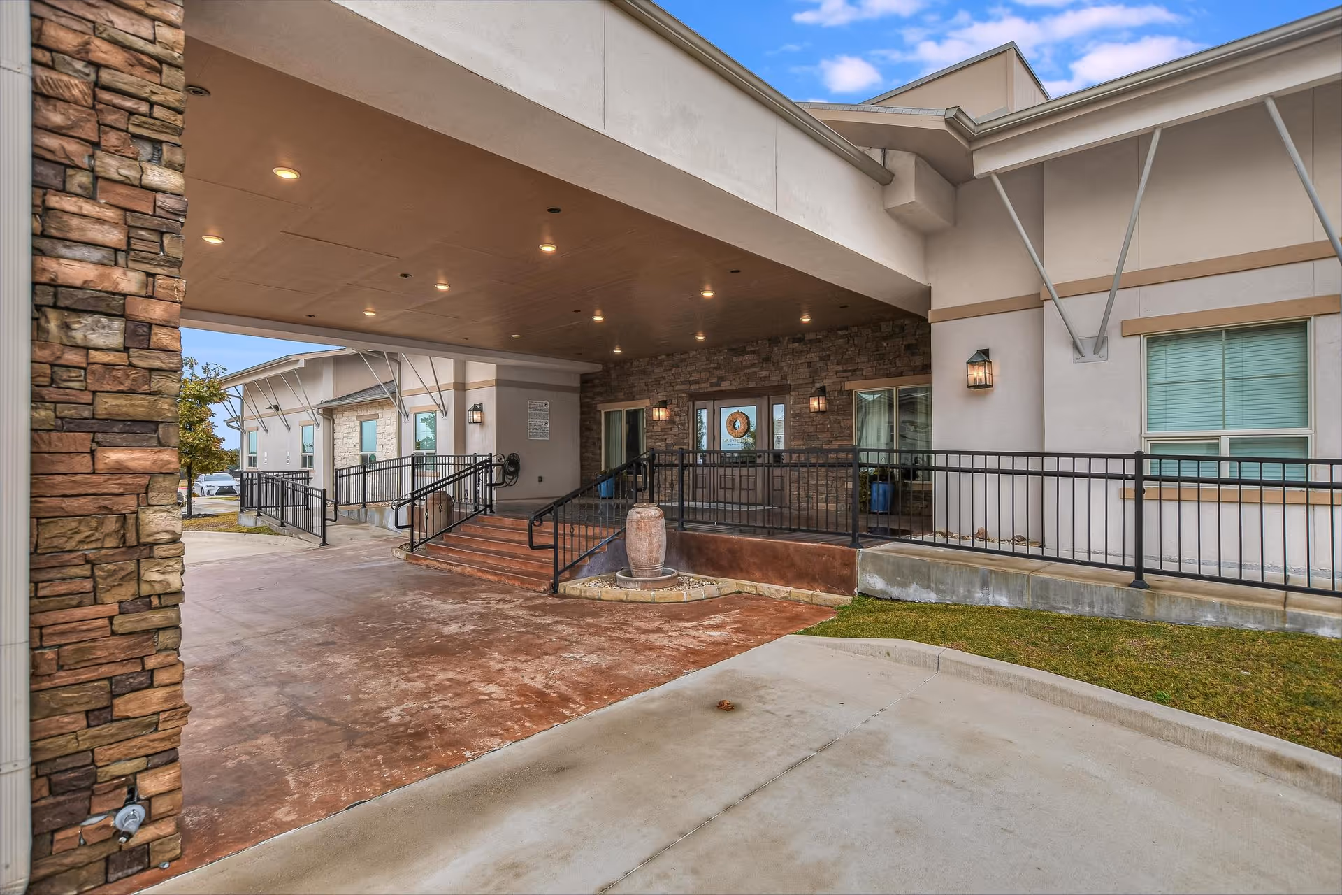 Covered entrance and porte-cochere of a memory care facility with ramps, stairs, railings and double glass doors.