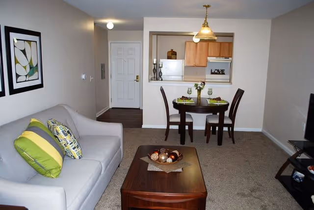 Living room view with a gray sofa, coffee table, small round dining table, and a pass-through to the kitchen.