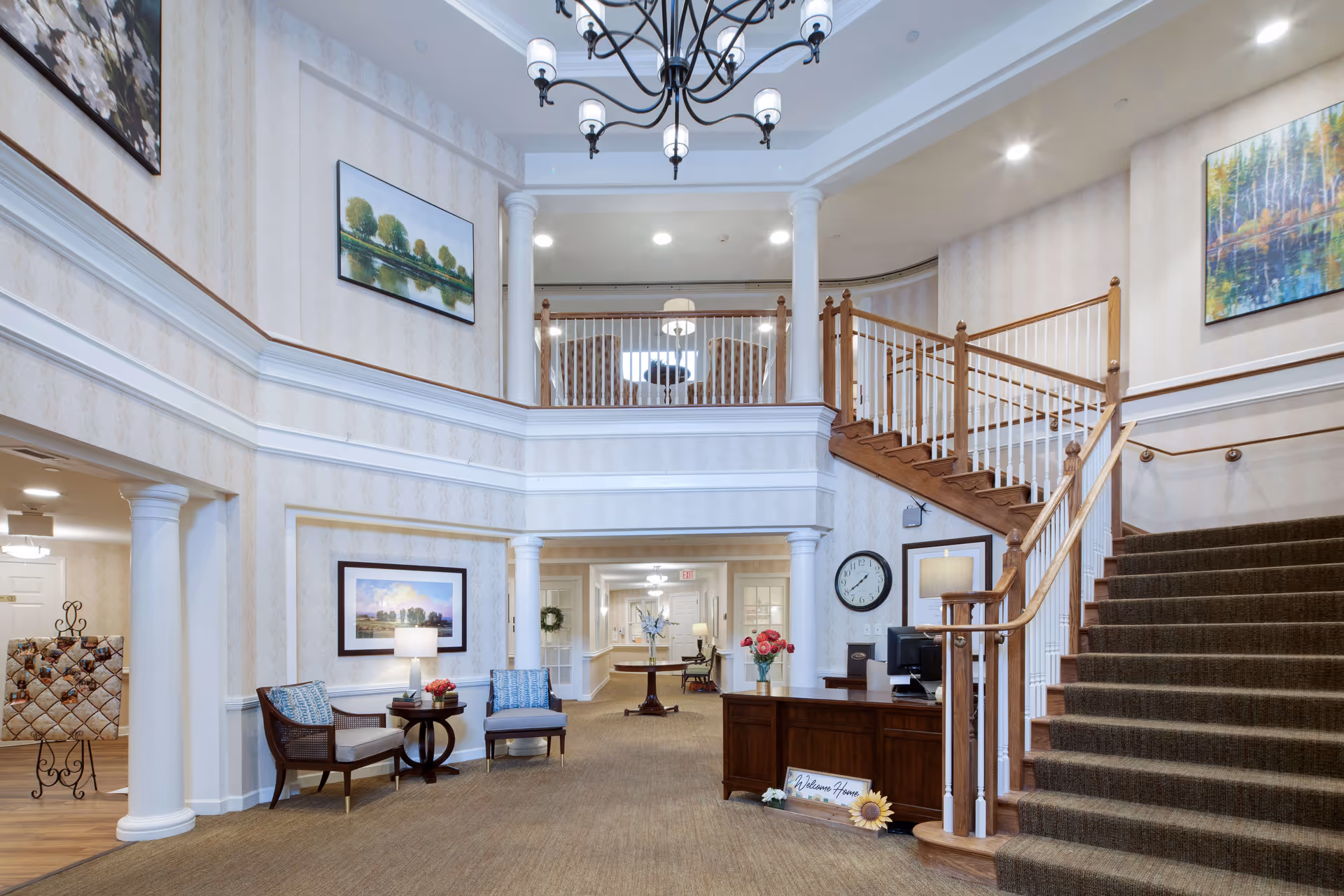 Spacious two-story reception lobby with a staircase, chandelier, seating area and front desk.